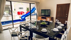 A dining area with a black table set for six, white chairs, and a view of a blue slide outside. - 8bdr Avoca Pool Villas 172 (Muang Pattaya)