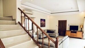 A spacious living area with a staircase, a sofa set, a television, and a cabinet. - 8bdr Avoca Pool Villas 172 (Muang Pattaya)