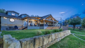 A modern house with a covered patio, stone retaining wall, and a well-lit outdoor area. - Packsaddle Paradise- Lakefront w/ Beach & Views (Kingsland)