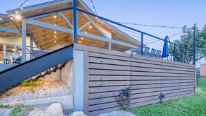 A modern building with a wooden deck, outdoor seating, and string lights. - Packsaddle Paradise- Lakefront w/ Beach & Views (Kingsland)