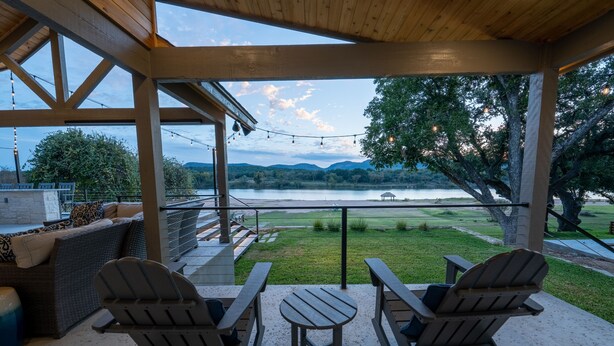 A covered patio with Adirondack chairs and a table, overlooking a lake and grassy area. - Packsaddle Paradise- Lakefront w/ Beach & Views (Kingsland)
