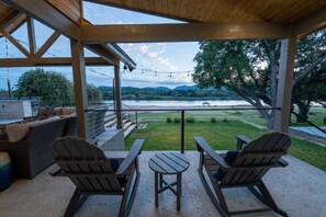 Un porche cubierto con sillas Adirondack y una mesa, con vistas a un lago y una zona verde.