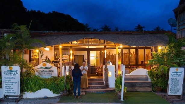 Un spa avec une enseigne traditionnelle indiquant qu'on y propose des massages thaïlandais, une statue et une entrée bien éclairée.