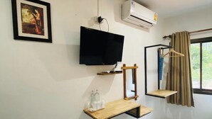 Une pièce équipée d’un téléviseur fixé au mur, d’un appareil de climatisation, d’étagères en bois, d’un miroir et d’une fenêtre avec des rideaux.