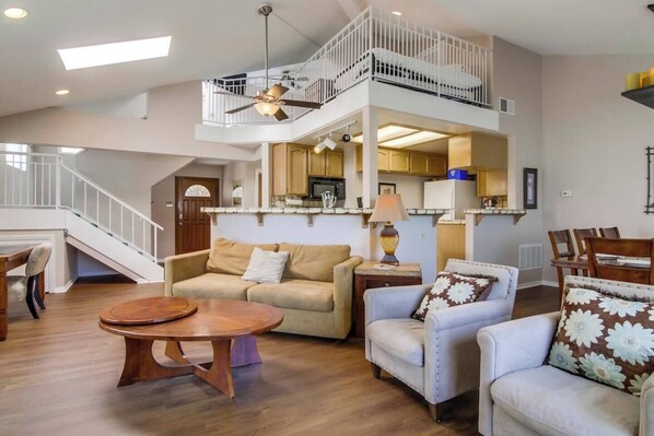 A spacious living area with a high ceiling, a dining table, and a kitchen area visible through an open layout.