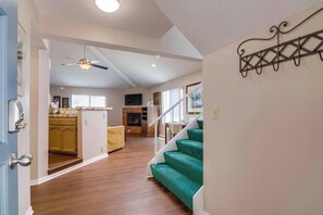 A spacious living area with a staircase, wooden flooring, and a ceiling fan.