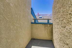 Corredor estreito com guarda-corrimão azul e vista para um terraço com um cone vermelho.