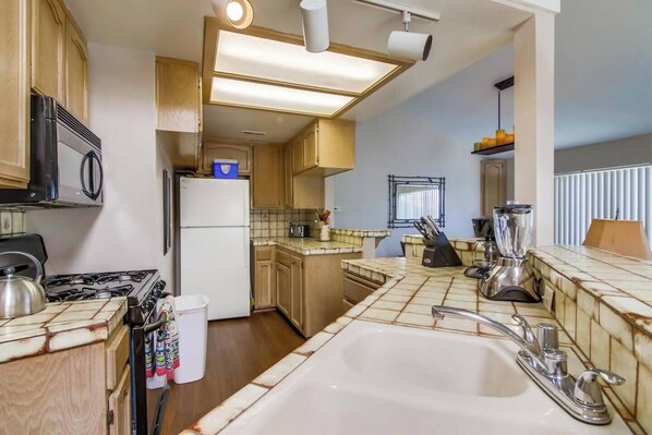 A compact kitchen with a gas stove, a white sink, and a built-in refrigerator.