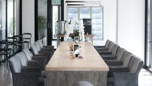 A modern conference room with a long table, grey upholstered chairs, a large pendant light, and a water dispenser in the background. - CREW Hotel (Chiang Mai)