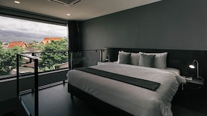 A modern bedroom with a large bed, a nightstand, a desk lamp, and a view of the city through a large window. - CREW Hotel (Chiang Mai)