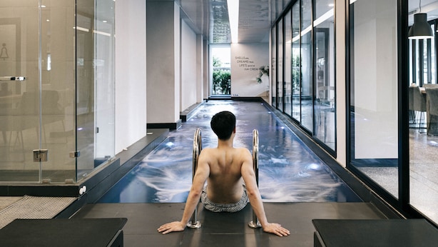 A modern interior with a glass wall, a person in a yoga pose, and a reflective floor. - CREW Hotel (Chiang Mai)