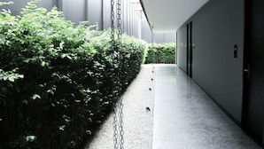 A hallway with a concrete floor, a chain-link fence on one side, and a door on the other. - CREW Hotel (Chiang Mai)