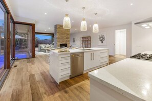 A modern kitchen with a central island, wooden flooring, and pendant lighting.