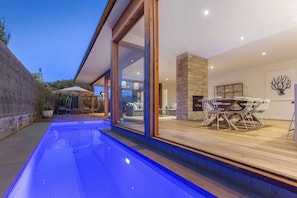 A modern outdoor pool area with a glass-enclosed dining space and a stone fireplace.