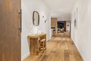 A hallway with wooden flooring, a wooden bench, a mirror, and a small table with a decorative item.