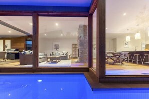 A modern interior with a pool, a living area with sofas and a dining area with a bar.