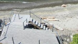 Une plage avec un voilier à l’horizon et une structure en bois près du bord de l’eau.