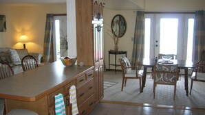 Un vaste espace de vie comprenant un îlot central, des meubles de rangement en bois, une table à manger avec des chaises et une grande fenêtre qui laisse entrer la lumière naturelle.