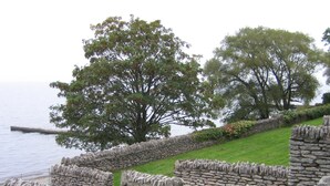 Un mur de pierres, avec une zone herbeuse et des arbres en arrière-plan.