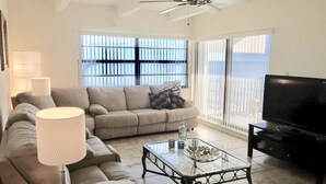 A living room with a sofa, a glass coffee table, a television, and a ceiling fan. - Oceanfront Condo With Incredible Views (Vero Beach)