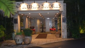 The entrance of KUIHNO SHORES with a tiled pathway, large potted plants, and a well-lit sign.