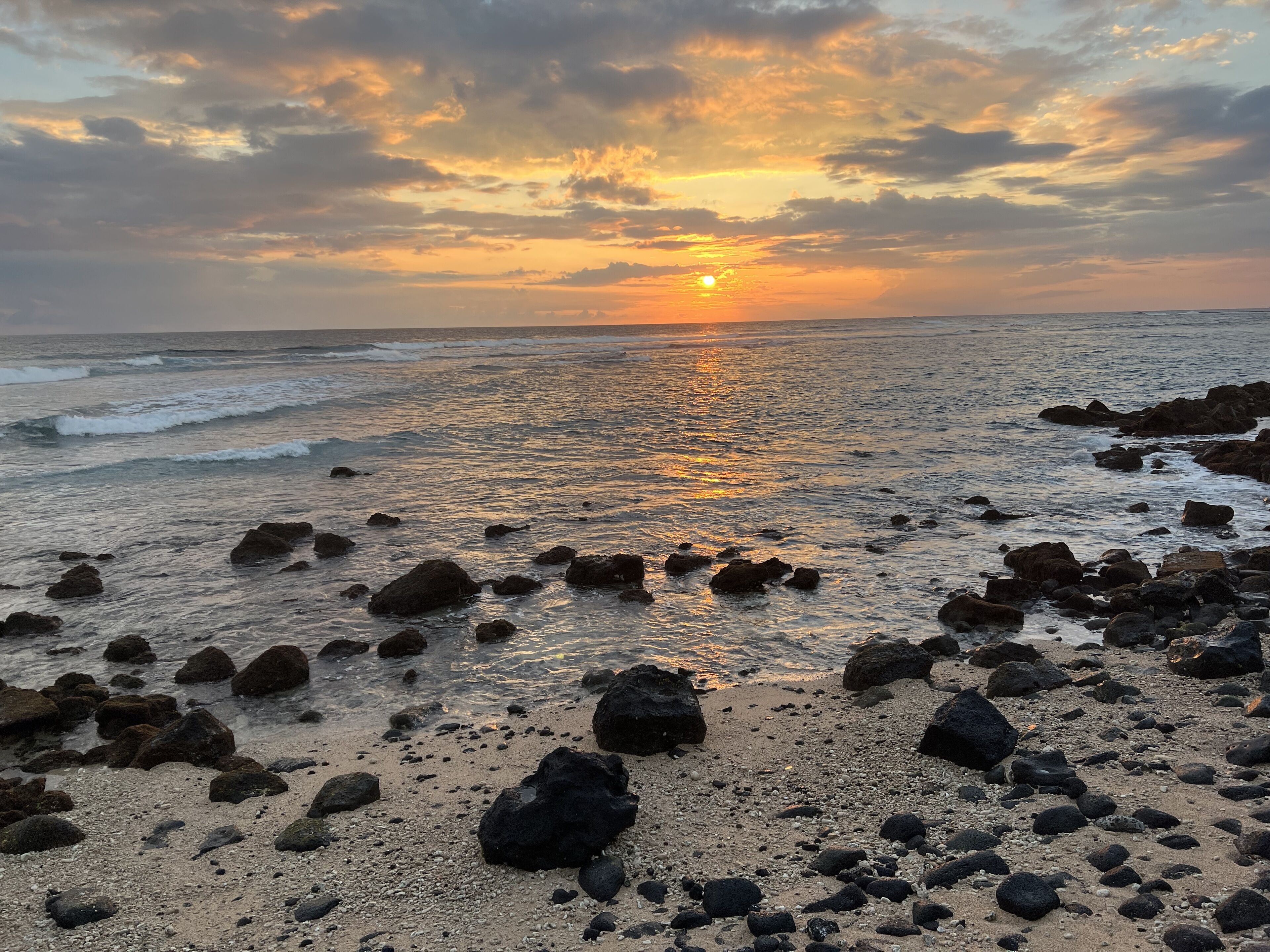 Una playa con rocas dispersas y una puesta de sol al fondo.