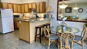 A kitchen with wooden cabinets, a refrigerator, a microwave, and a dining area with a glass table and wicker chairs.