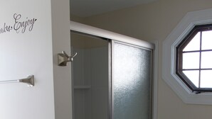 A bathroom with a glass shower enclosure, a patterned floor, and a window with a view.