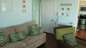 A living room with a beige sofa, a wicker chair, and a door leading to another room.