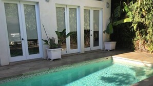 Una piscina con acqua cristallina, circondata da un solarium piastrellato e piante in vaso.
