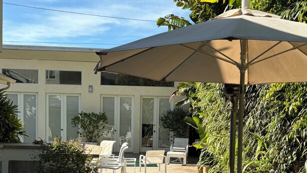Un'area patio con posti a sedere all'aperto, tra cui un tavolo rotondo e sedie, e un ombrellone grande che offre ombra.
