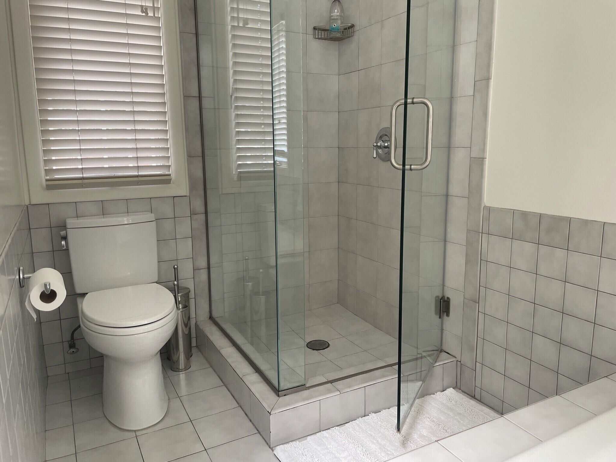 A bathroom with a toilet, a glass-enclosed shower, and a white tiled floor.