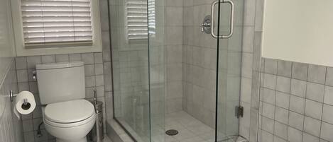 A bathroom with a toilet, a glass-enclosed shower, and a white tiled floor.