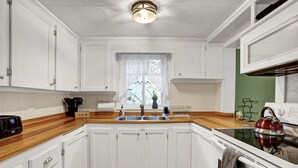 Een keuken met witte kastjes, een houten aanrecht, een fornuis en een spoelbak.