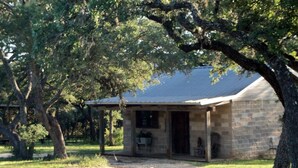 A stone building with a covered porch, surrounded by trees. - Private, Cozy Cabin on 6 acres with Mountain Views in the Heart of the Texas Hill Country Near Lost Maples and Garner State Parks (Vanderpool)