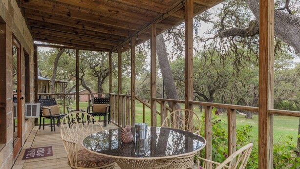 A covered outdoor seating area with a round table and chairs, a wooden deck, and a view of a wooded area. - Private, Cozy Cabin on 6 acres with Mountain Views in the Heart of the Texas Hill Country Near Lost Maples and Garner State Parks (Vanderpool)