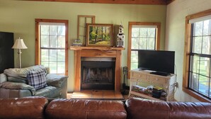 A cozy living room with a fireplace, leather sofa, and a television on a stand. - Private, Cozy Cabin on 6 acres with Mountain Views in the Heart of the Texas Hill Country Near Lost Maples and Garner State Parks (Vanderpool)