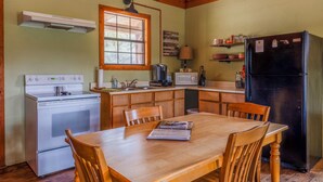A compact kitchen with a stove, microwave, refrigerator, wooden table, and chairs. - Private, Cozy Cabin on 6 acres with Mountain Views in the Heart of the Texas Hill Country Near Lost Maples and Garner State Parks (Vanderpool)