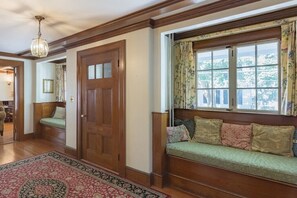 A traditional room with a wooden door, a bench with cushions, a patterned rug, and a window with floral curtains. - Charming downtown home in the center of Historic Marblehead: 5min walk to harbor (Marblehead)