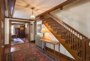 A grand staircase with wooden balusters and a chandelier, leading to a room with a patterned rug and a table with a lamp. - Charming downtown home in the center of Historic Marblehead: 5min walk to harbor (Marblehead)