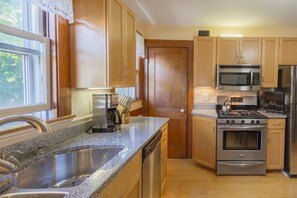 A kitchen with wooden cabinets, a stainless steel sink, a microwave, a stove, and a kettle. - Charming downtown home in the center of Historic Marblehead: 5min walk to harbor (Marblehead)