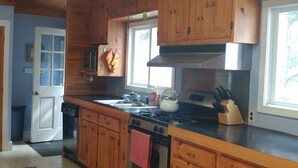 A kitchen with wooden cabinets, a stove, and a window. - Remarkable Four Gable House Overlooking Friendship Harbor (Friendship)