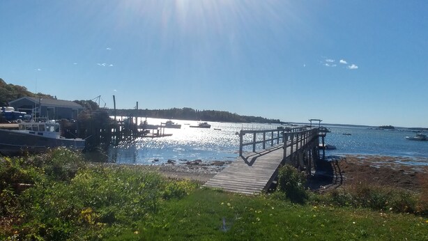A wooden pier extending into a calm body of water with boats docked nearby. - Remarkable Four Gable House Overlooking Friendship Harbor (Friendship)