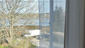 A room with a wooden bench, a large window with sheer curtains, and a view of a parking lot with vehicles. - Remarkable Four Gable House Overlooking Friendship Harbor (Friendship)
