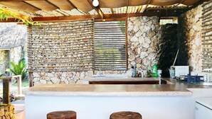 Een rustieke keuken met een stenen muur, houten plafond en een bar met krukken.