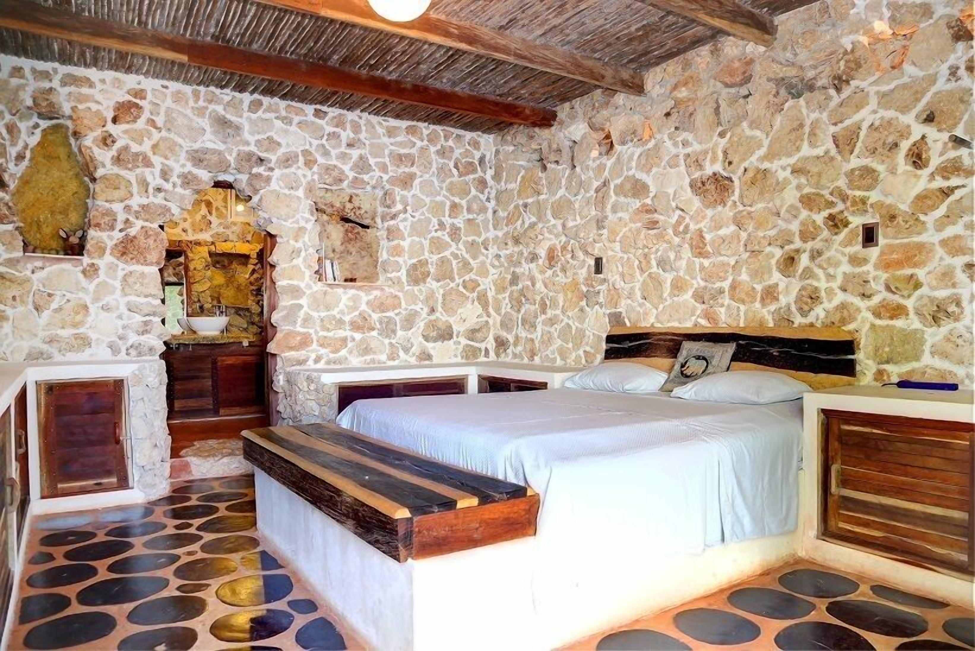 A stone-walled bedroom with a bed, bench, and a small altar.