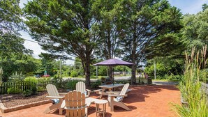 Un patio exterior con sillas Adirondack, una mesa y un paraguas morado.