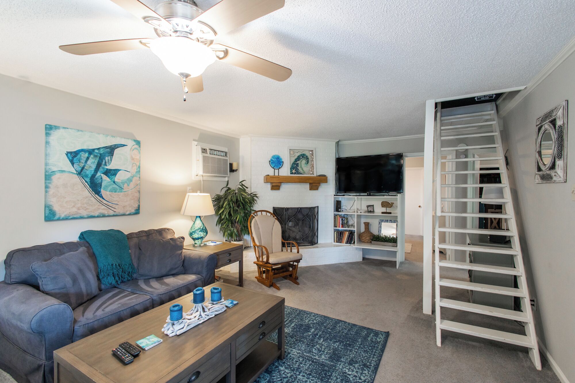 A living room with a ceiling fan, a sofa, a coffee table, a TV, and a bookshelf.