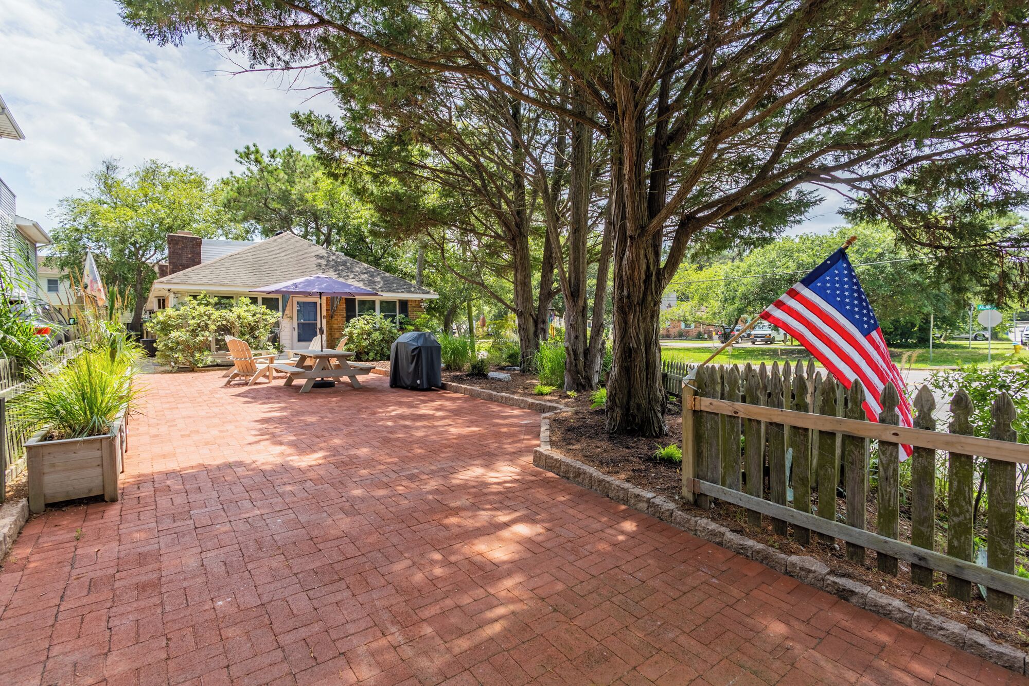 A patio area with a brick walkway, a covered table and chairs, and a flag.