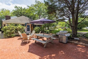 Un patio con una parrilla, sillas y una mesa.